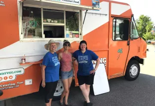 Three people stand in front of the bright-orange-and-white Wong Way Veg food truck in Denver