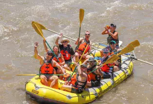 Participants hold their paddles up while sitting on a yellow raft during Big Gay Raft Trip in Glenwood Springs