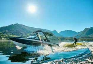 A water skier hits big waves on glassy, grand lake,= with mountains rising behind him