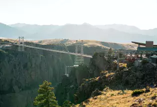 A valley of trees under the Royal Gorge Bridge in Cañon City. In the background is a landscape of faded blue mountains against the skyline.