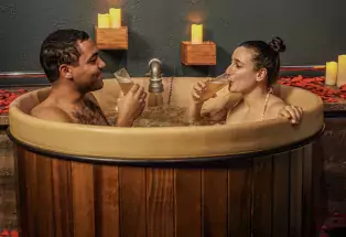 Two people sit in a tub and drink beer pints at the Denver Beer Spa