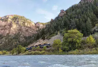 The Rocky Mountaineer train travels alongside the rushing Colorado River as the sun sets behind a rocky outcrop