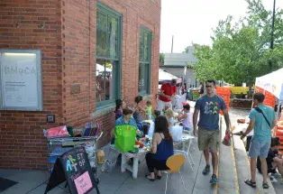 At BMoCA Art Stop, kids sit on tables in front of the museum doing various crafts