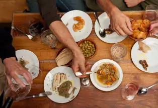 Four diners' hands reach for small plates Cafe Aion in Boulder in a birds-eye view of the wood table stacked with dishes