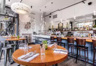 White subway tile, warm-wood tables and empty bar stools await patrons