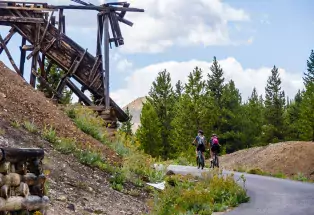 Two people bike a paved trail that passes old mining artifacts on the Mineral Belt Trail in Leadville, Colorado