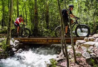 Two people bike over a bridge that crosses a rushing creek in the forest near Leadville and Twin Lakes, Colorado