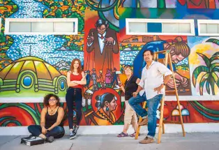 Four artists stand in front of a vibrant mural mural along Pueblo's Creative Corridor
