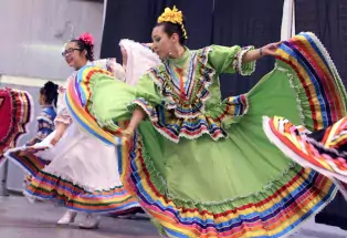 A woman in a bright green dress twirls her skirt in a dance performance at downtown Greeley's Cinco de Mayo celebration