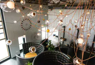 A tangle of lights hung by copper wires looks over black-leather booths