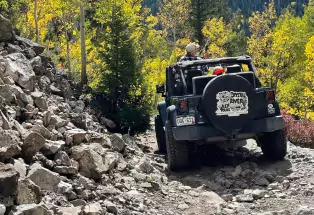 A Jeep rumbles down a rocky mountain road through a forest in Marble, Colorado
