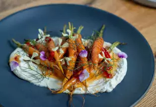 A blue plate holds mini carrots topped with purple flowers
