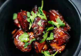 A black bowl holds a reddish dish of spicy pork topped by bright green cilantro