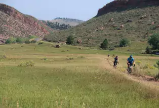 Gravel bikers cycling on a trail through green prairie grasses with the mountains in the background in Fort Collins, Colorado
