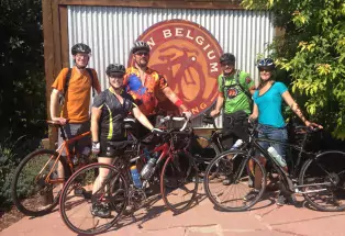 Five people in biking attire pose for a photo at New Belgium Brewing Companyin Fort Collins. They wear helmets and hold their bikes.