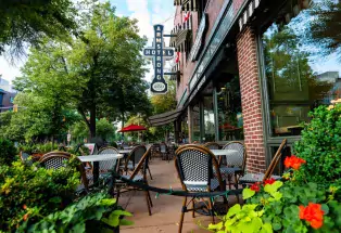 A photo of an empty patio seating outside of a brick-and-window-covered building that reads "ARMSTRONG HOTEL" on the side. There are various plants and bright-red flowers around the restaurant's patio. The restaurant is the Ace Café on College Avenue in downtown Fort Collins.