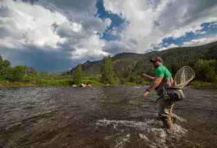 A person with waders and a net fly-fishees from a rock in the middle of the rushing Cache la Poudre River in Fort Collins, Colorado