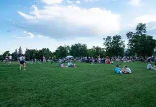 People at the FoCo Food Truck Rally in Fort Collins, Colorado sitting on blankets on an emerald-green lawn under a cloud-streaked blue sky