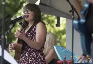 A person at a microphone sings and plays guitar at the Lagoon Concert Series in Fort Collins, Colorado