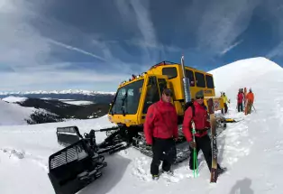 Group of skiers standing by a snowcat on a mountain top