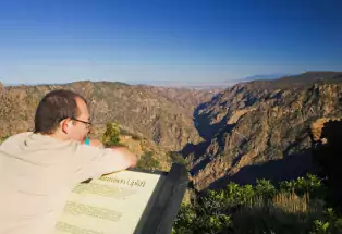 A person leans over an interpretive sign and gazes into the distance at the striped walls of the Black Canyon of the Gunnison National Park near Montrose, Colorado