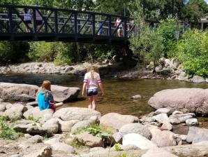 Things to Do with Kids in Boulder Children playing in Boulder Creek with pedestrian bridge overhead.