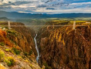 Royal Gorge Bridge & Park Royal Gorge Bridge & Park: Golden hour with Arkansas River snaking through rock walls of the gorge with the metal suspension bridge across the upper part of the canyon.
