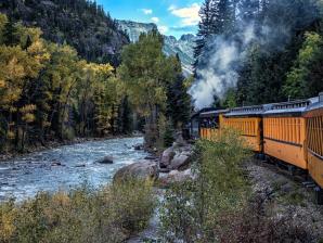 History and scenic beauty on the Durango & Silverton Narrow Gauge Railroad The Durango Train runs alongside a river in a canyon where the trees are just turning gold for autumn