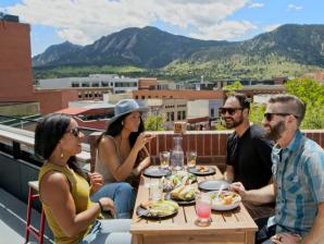 A group of four people eating on a rooftop in Boulder with the Flatirons in the background