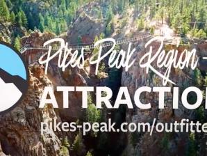 Pikes Peak Region Attractions Broadmoor Outfitters in Colorado Springs White text that says "Pikes Peak Region Attractions" with a website beneath it. Beside the text is a circular logo with a drawing of white mountains beneath blue sky. Behind the text and logo is a rope ladder stretched across and over a couple of deep valleys. The cliff tops are covered in bright green pine trees.